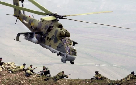 An HD desktop wallpaper showing a Mil Mi-24 military helicopter flying over soldiers deployed on a hillside.