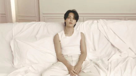 HD desktop wallpaper featuring BTS member Jimin in a serene setting, dressed in white, sitting on a couch with a thoughtful expression.
