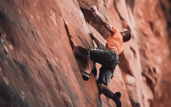 Dynamic HD wallpaper of a rock climber ascending a steep red cliff, showcasing determination and adventure for desktop backgrounds.