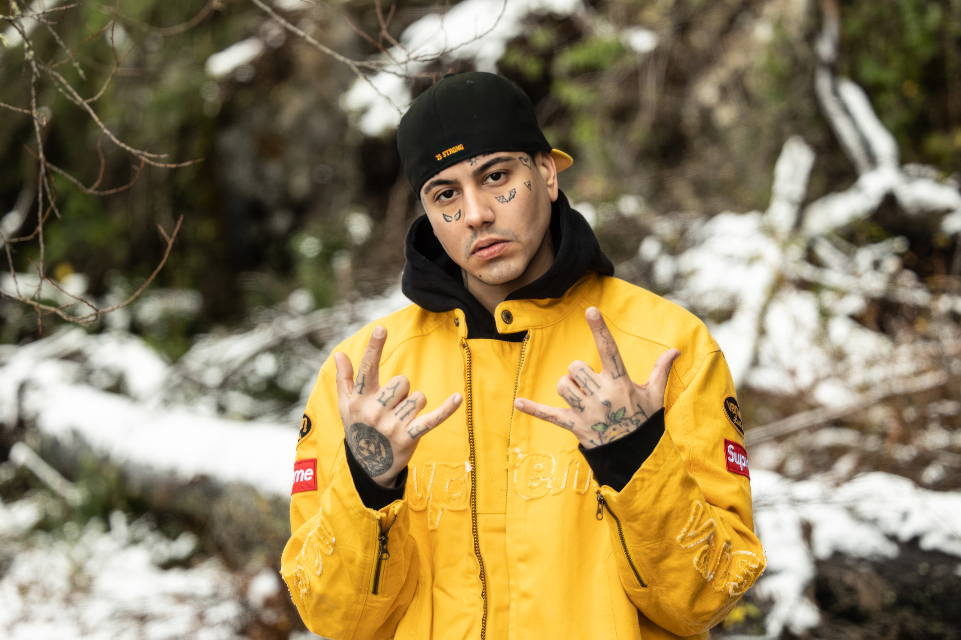 HD wallpaper of a person posing confidently in a yellow jacket against a snowy forest backdrop, symbolizing music artist Duki.