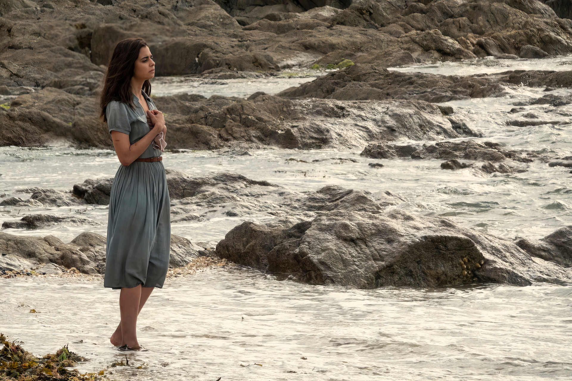 HD desktop wallpaper featuring a contemplative character from the TV Show 'All the Light We Cannot See' standing by the seaside with rocks in the background.