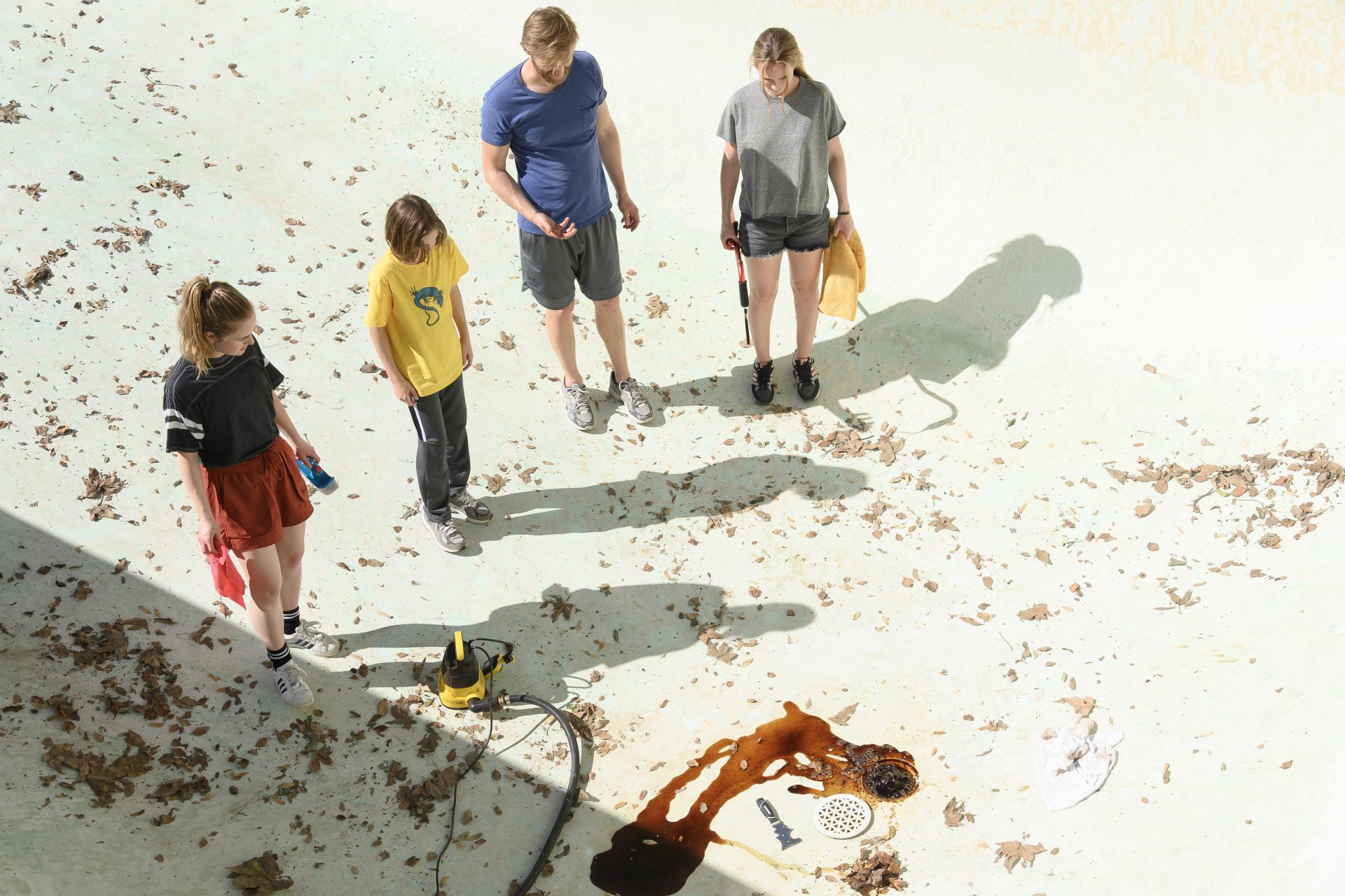 A scene from the movie *Night Swim*, featuring four young people examining a pool with debris scattered around, set against a bright, sunlit background. HD wallpaper quality.