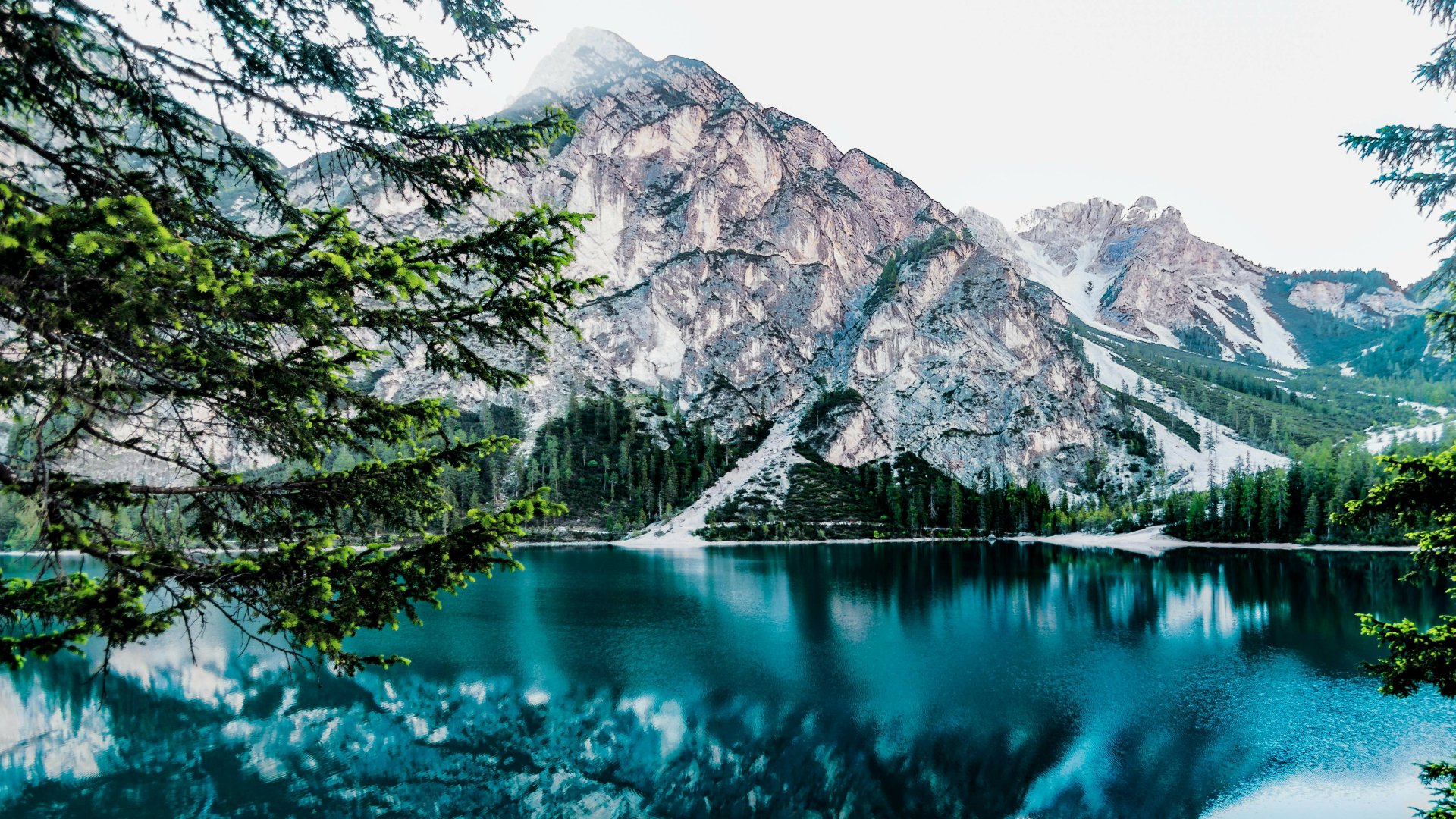 4K Ultra HD desktop wallpaper featuring a serene mountain landscape reflected in a clear lake, framed by lush green trees under a bright sky.