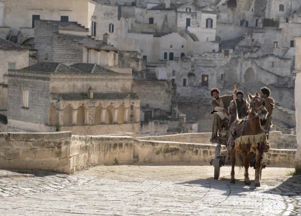 High-definition desktop wallpaper featuring a scene from 'The Book of Clarence' with characters on a horse-drawn cart in an ancient town setting.
