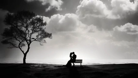 A black-and-white image of a couple sharing a romantic kiss on a bench, silhouetted against a dramatic sky, with a solitary tree in the background. This HD desktop wallpaper captures deep emotion.