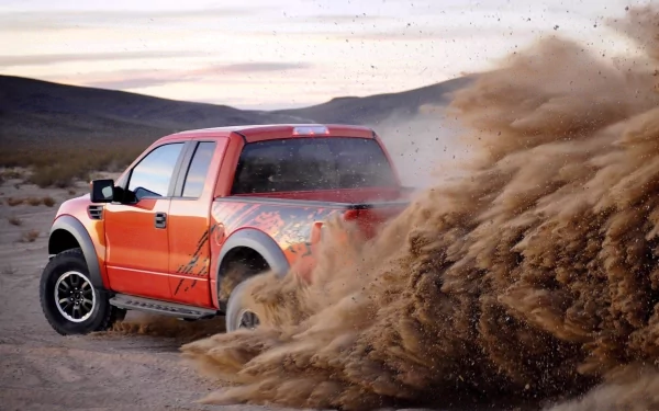 Red Ford Raptor kicking up dirt on a rugged desert trail, captured in a high-definition PC desktop wallpaper.