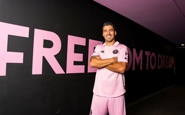 Professional soccer player sporting the Inter Miami CF kit, posing confidently in front of a pink 'FREEDOM TO DREAM' slogan, suitable as an HD desktop wallpaper for sports fans.