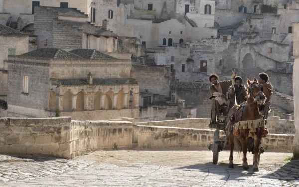 High-definition desktop wallpaper featuring a scene from 'The Book of Clarence' with characters on a horse-drawn cart in an ancient town setting.
