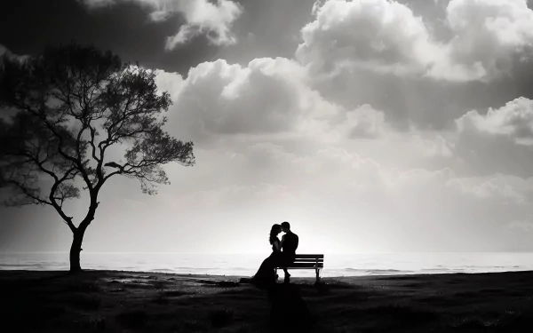 A black-and-white image of a couple sharing a romantic kiss on a bench, silhouetted against a dramatic sky, with a solitary tree in the background. This HD desktop wallpaper captures deep emotion.