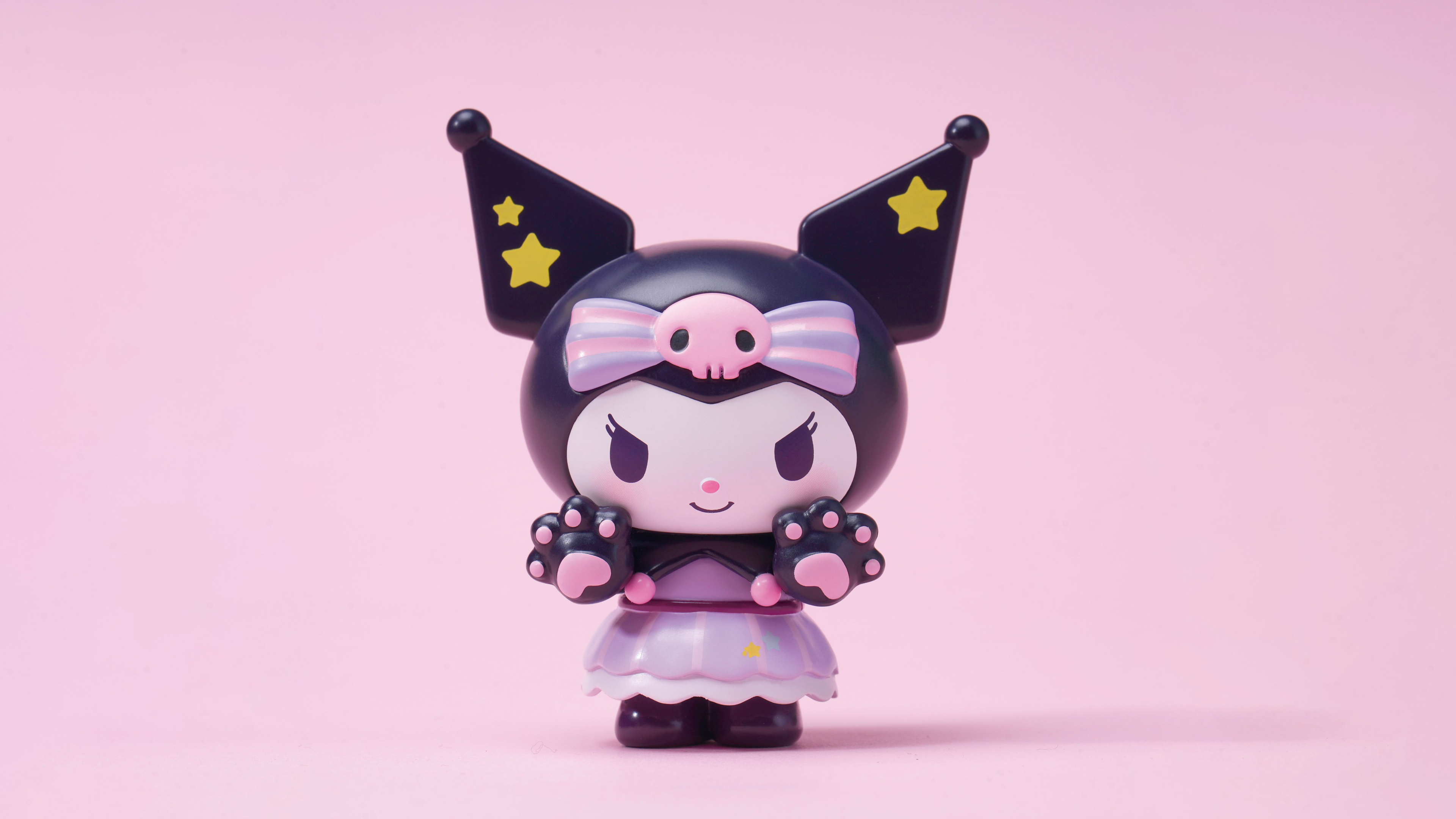 HD wallpaper of Kuromi from Onegai My Melody anime, featuring the character in her signature black jester hat with pink accents and star details, on a pastel pink background suitable for desktops.