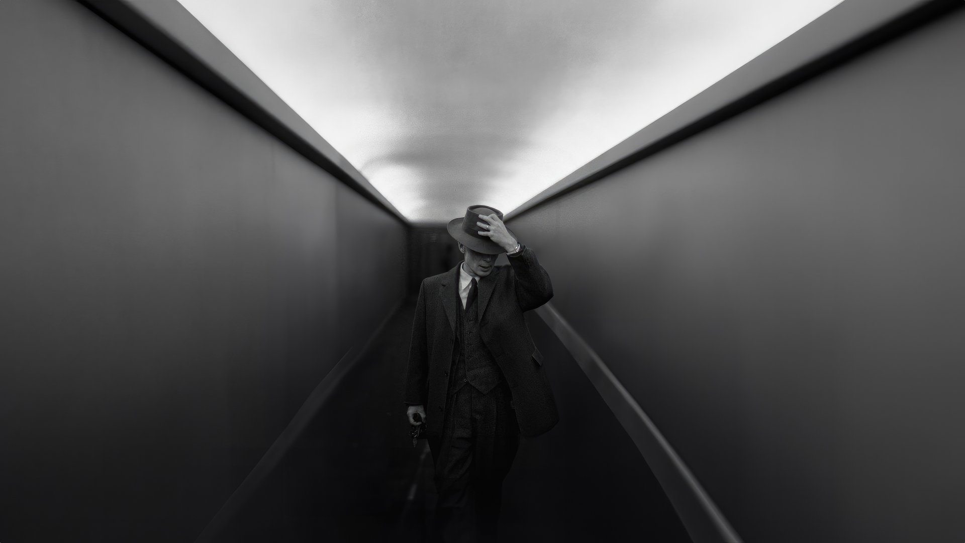 Monochrome HD wallpaper featuring a man dressed in 20th-century attire walking down a dramatic corridor, evoking themes from the movie Oppenheimer.