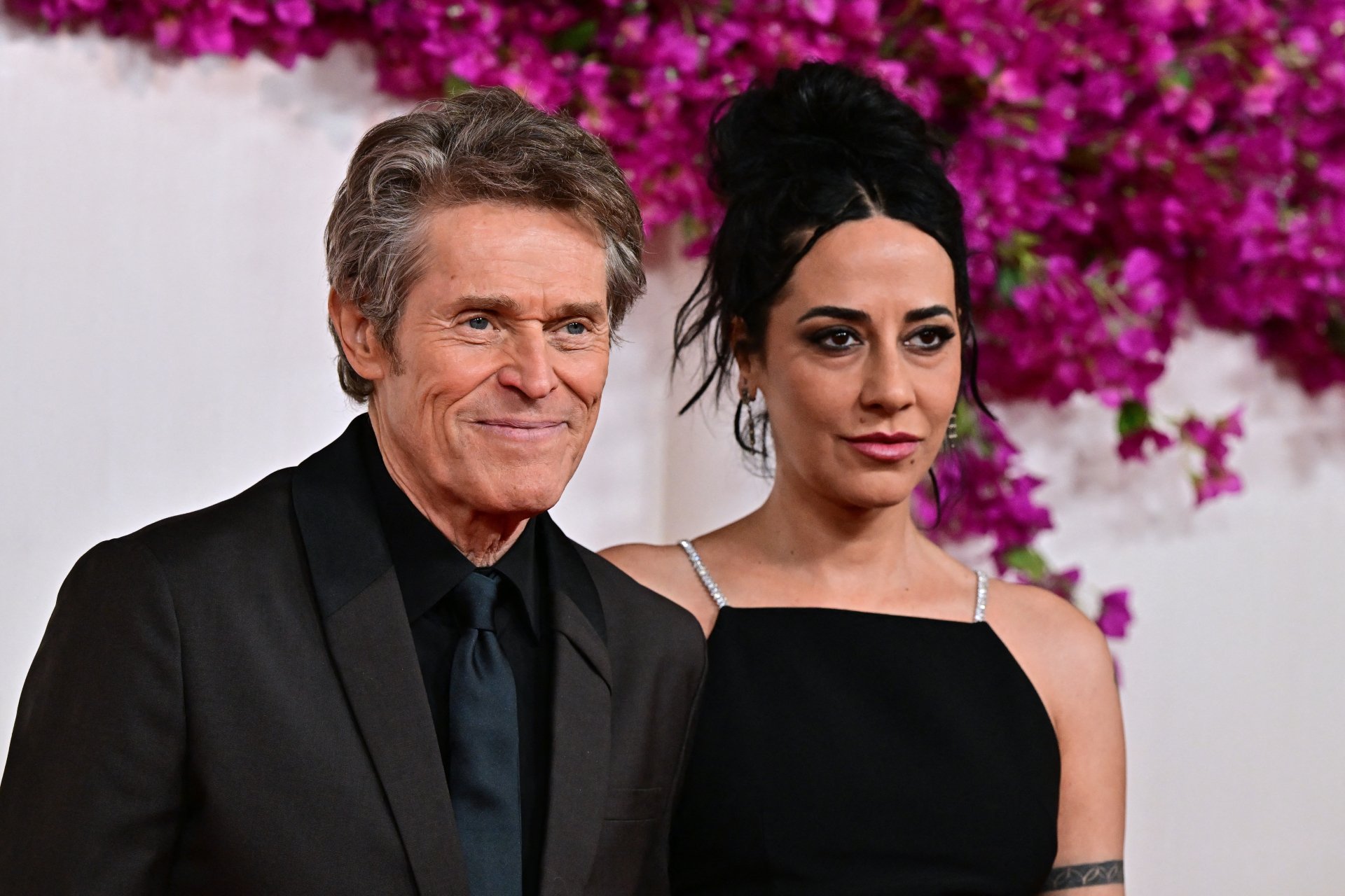 A man and woman posing together at the Academy Awards, with a pink floral background behind them. The man is wearing a black suit and the woman is in a black dress. This image serves as a high-definition desktop wallpaper or background.
