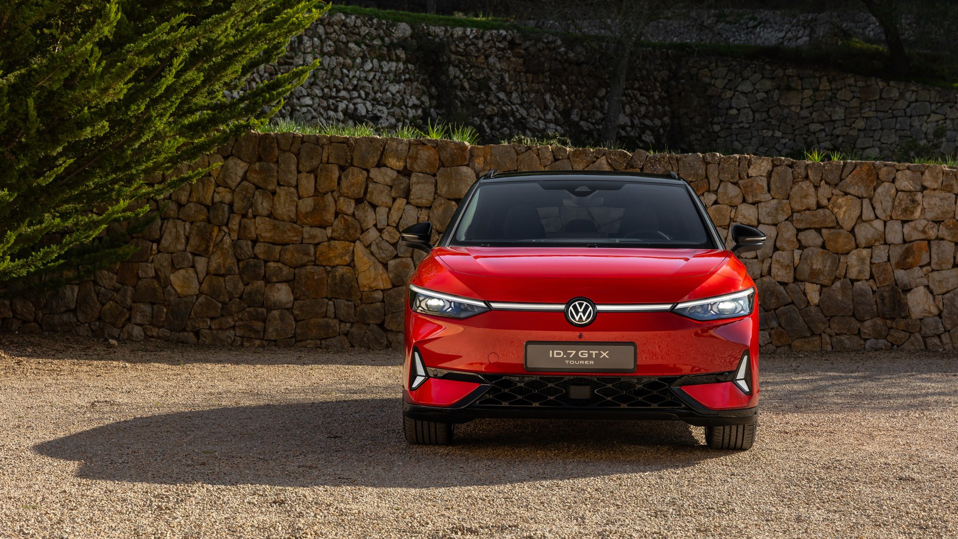 A stunning HD wallpaper featuring the Volkswagen ID.7 GTX Tourer, showcasing its sleek design and bold red color against a rustic stone backdrop.