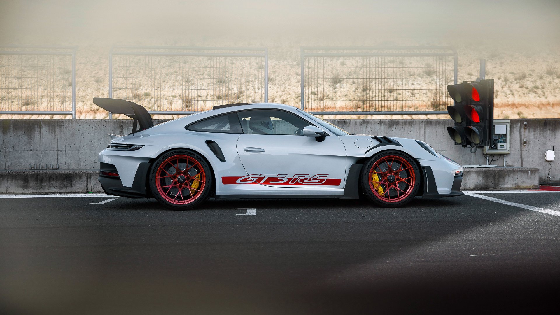 High-definition image of a Porsche 911 GT3 RS parked at a traffic light, showcasing its sleek design and vibrant red accents against a blurred background.