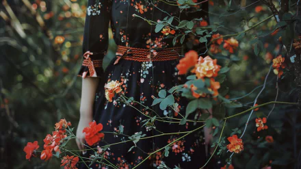 HD wallpaper featuring a person in a black floral dress amidst lush greenery with vibrant orange flowers.