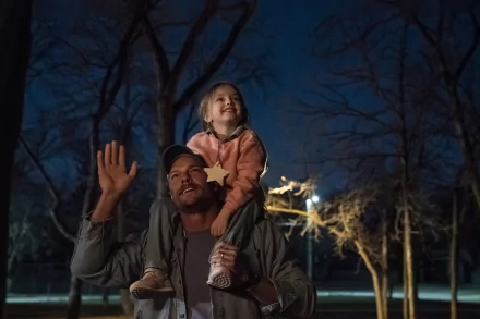 HD desktop wallpaper depicting a heartwarming scene from the movie Ordinary Angels with a man holding a joyful child on his shoulders at dusk.