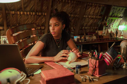 Jessica Williams as a character in the 2024 movie Road House, featured in a HD desktop wallpaper, sitting thoughtfully at a desk with a laptop and various items.