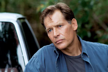 HD desktop wallpaper of a character from the TV show Dexter with a contemplative expression, standing by a car in a forested area.