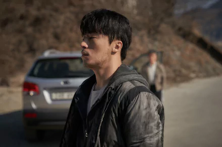 HD desktop wallpaper from the TV Show Parasyte: The Grey featuring a pensive man in the foreground with another person and a car in the background.