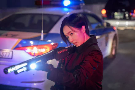 A character from the TV show Parasyte: The Grey in a red jacket aiming a futuristic weapon, with a police car's flashing lights in the background. This image serves as an HD desktop wallpaper and background.