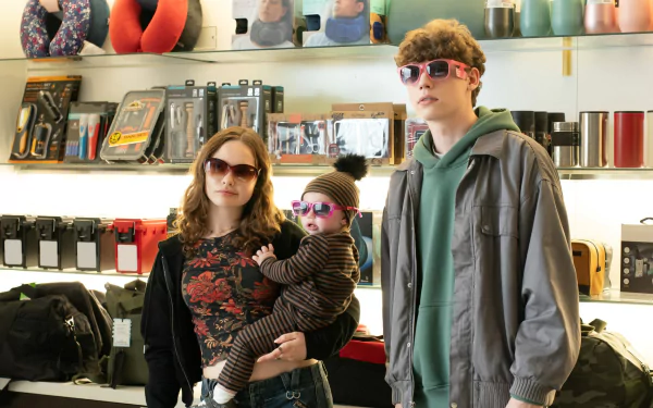 HD desktop wallpaper from the movie The Family Plan featuring two adults with sunglasses and a baby in a store.