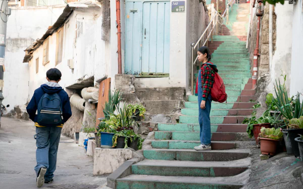 HD desktop wallpaper featuring a scene from the movie Past Lives with two individuals on a stairway amidst an old residential area.