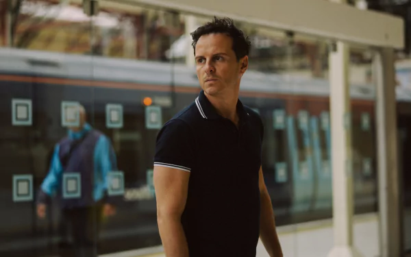 A scene from the movie *All of Us Strangers*, featuring a man in a dark polo shirt, gazing thoughtfully while standing near a train station backdrop. HD desktop wallpaper and background.