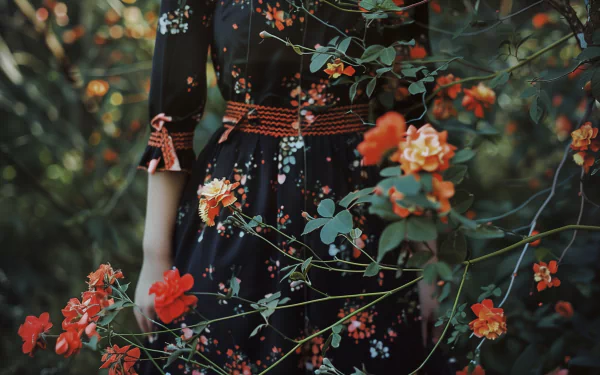 HD wallpaper featuring a person in a black floral dress amidst lush greenery with vibrant orange flowers.