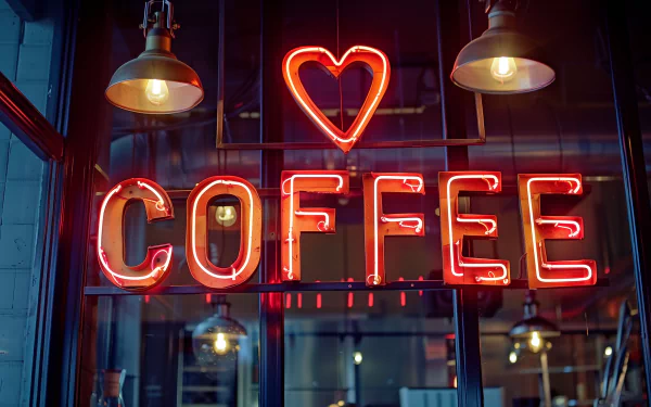 A vibrant neon sign reading COFFEE with a heart, hanging in a stylish café, creates an inviting atmosphere. This HD wallpaper adds a warm touch to any background.