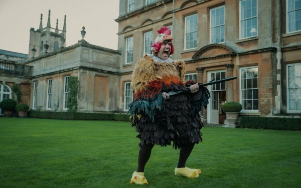 Quirky costume from The Gentlemen (2024) TV show showcased in an HD desktop wallpaper featuring a character dressed as a colorful bird in front of an elegant manor house.