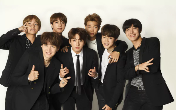 A high-definition desktop wallpaper featuring the members of BTS, dressed in stylish black suits, smiling and posing together for a vibrant music-themed background.