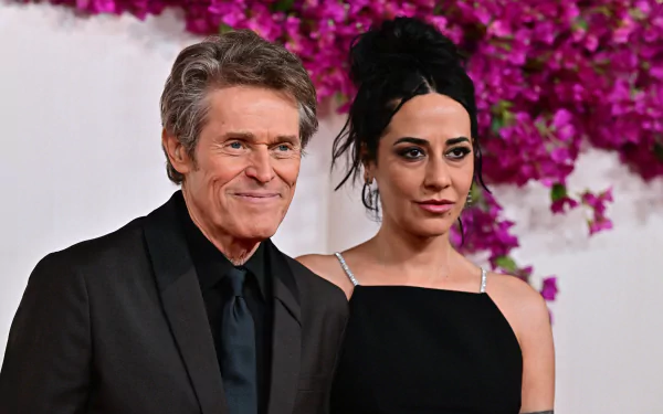 A man and woman posing together at the Academy Awards, with a pink floral background behind them. The man is wearing a black suit and the woman is in a black dress. This image serves as a high-definition desktop wallpaper or background.