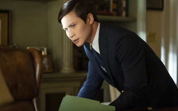 HD wallpaper from the TV show The Sympathizer featuring a character in a suit leaning over a desk with papers, with a vintage aesthetic.