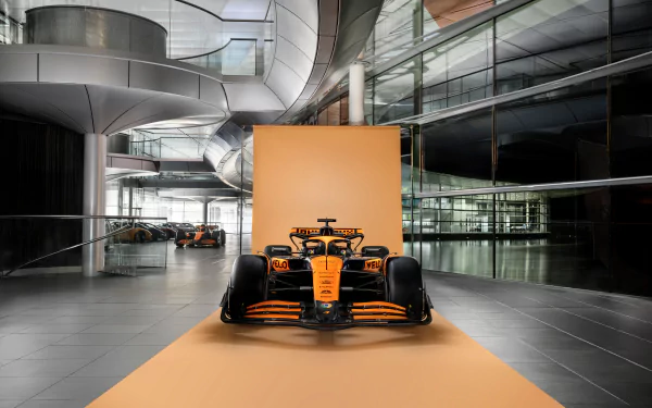 HD desktop wallpaper featuring the McLaren MCL38 Formula 1 car displayed in a modern, architectural venue with reflective surfaces.