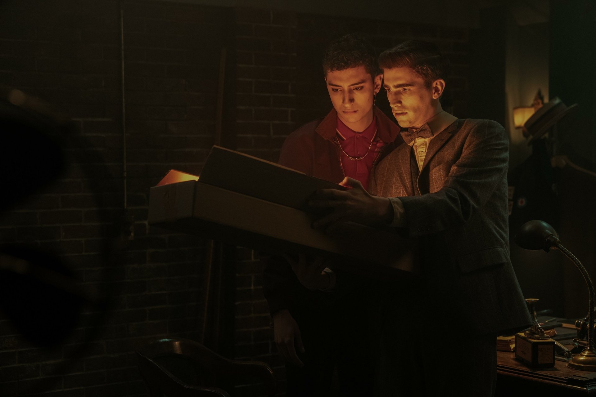 HD desktop wallpaper from the TV show Dead Boy Detectives featuring two young male characters examining a document in a dimly lit room.