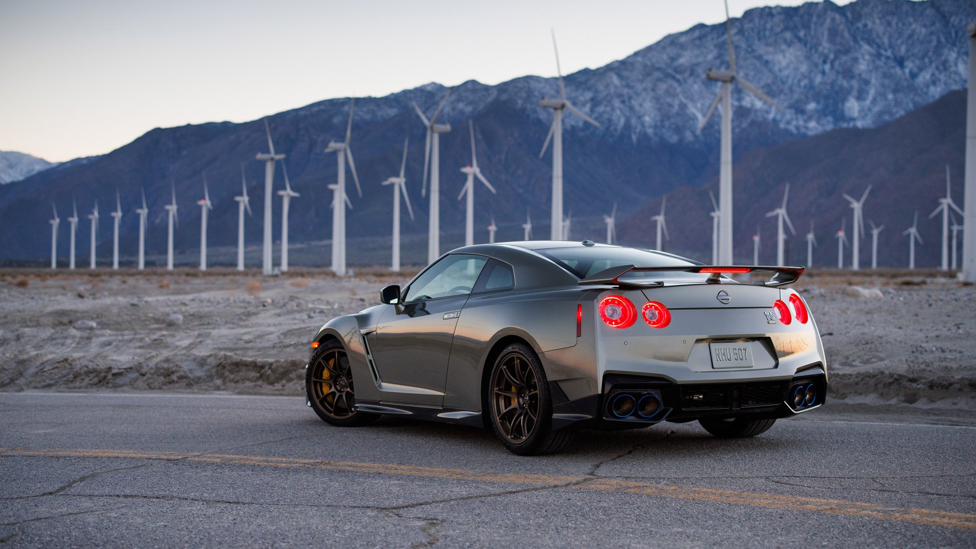 HD wallpaper of a Nissan GT-R parked on a road with a backdrop of wind turbines and mountains.