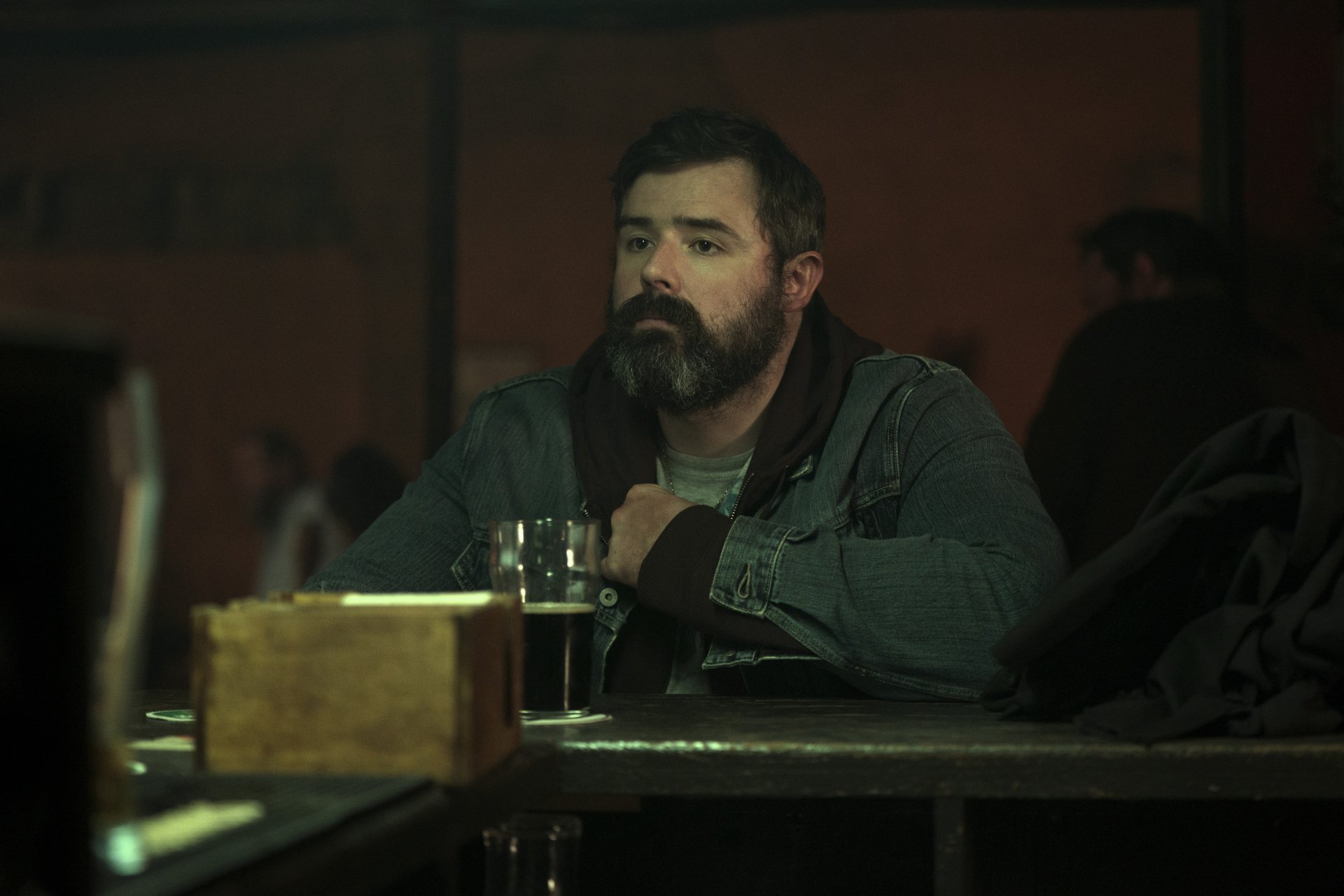 HD desktop wallpaper from the TV show Bodkin featuring a man with a beard sitting at a bar with a drink.