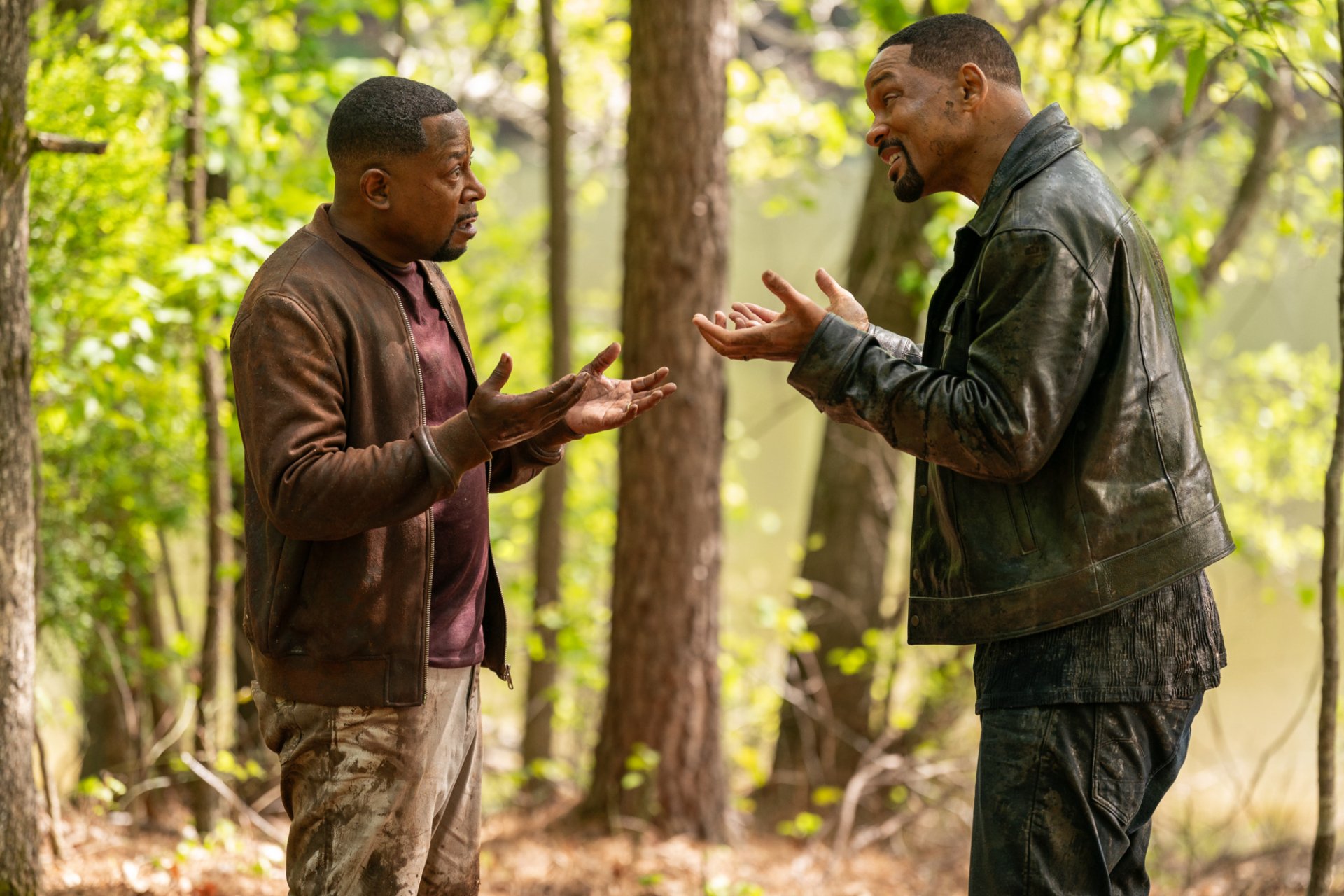 HD desktop wallpaper from the movie Bad Boys: Ride or Die featuring Will Smith and Martin Lawrence in a forest setting, engaging in an animated conversation.