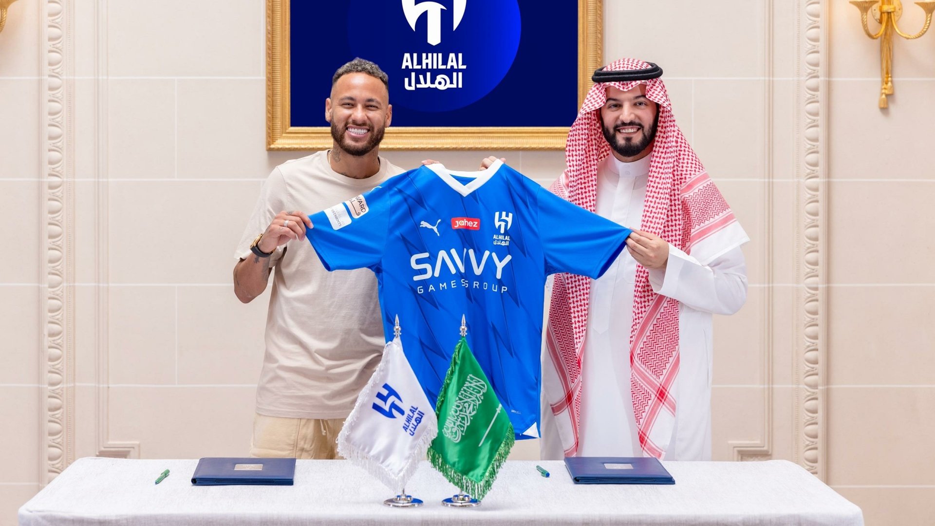 HD wallpaper and background featuring soccer star Neymar holding an Al Hilal jersey alongside a man in traditional attire. The setting includes Al Hilal branding in the background.