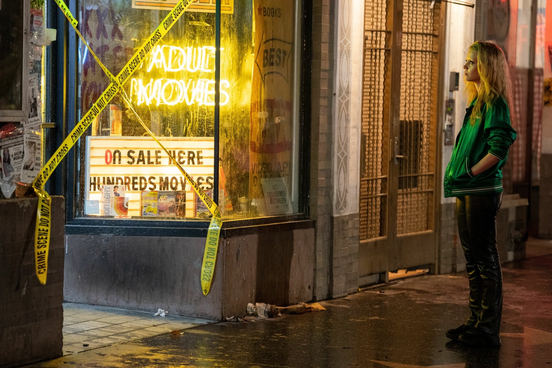 HD desktop wallpaper featuring Mia Goth as Maxxxine, standing in front of a neon-lit adult movie store at night, surrounded by yellow caution tape.