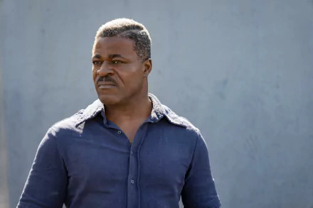 An intense-looking man in a blue shirt stands with a serious expression, possibly a scene from the movie The Ministry of Ungentlemanly Warfare, suitable as an HD desktop wallpaper and background.