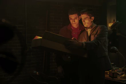 HD desktop wallpaper from the TV show Dead Boy Detectives featuring two young male characters examining a document in a dimly lit room.
