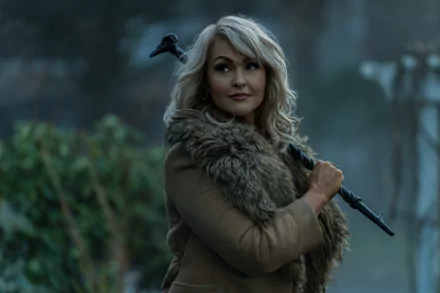 HD desktop wallpaper from the TV show Dead Boy Detectives featuring a woman in a fur jacket with a crow on her shoulder, holding a stick, set in a misty, eerie environment.