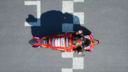 HD desktop wallpaper from MotoGP 24, featuring an overhead view of a racer on a red motorcycle crossing the finish line.