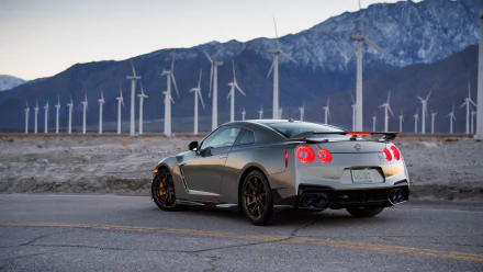 HD wallpaper of a Nissan GT-R parked on a road with a backdrop of wind turbines and mountains.