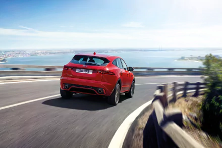 HD desktop wallpaper of a red Jaguar E-Pace driving on a coastal road with a scenic ocean view in the background.