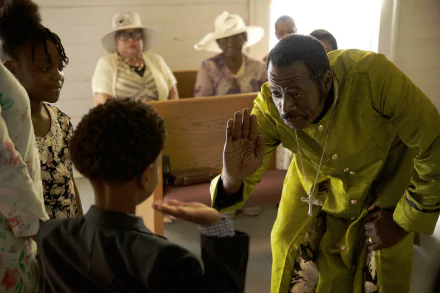 A scene from the movie Sound of Hope: The Story of Possum Trot, featuring a man in a green outfit interacting with a young boy in a church setting. The wallpaper is in HD quality.