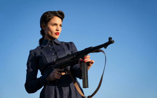 A woman in a vintage military-style outfit holding a submachine gun against a clear blue sky, conveying a theme related to the movie The Ministry of Ungentlemanly Warfare. Used as a high-definition desktop wallpaper and background.