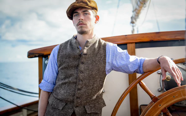 A man in period clothing stands by a ship's wheel with the ocean in the background, from the movie The Ministry of Ungentlemanly Warfare, suitable as an HD desktop wallpaper.