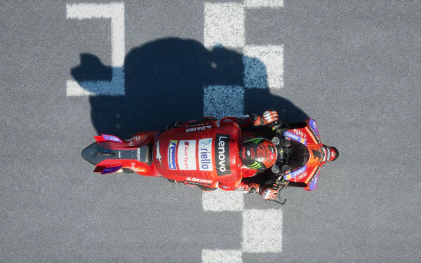 HD desktop wallpaper from MotoGP 24, featuring an overhead view of a racer on a red motorcycle crossing the finish line.